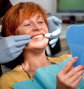 Woman smiling during dental cleaning, showcasing bright teeth, while a dental professional uses a scaler, emphasizing preventive care and oral health at Lexington Dental of Owasso.