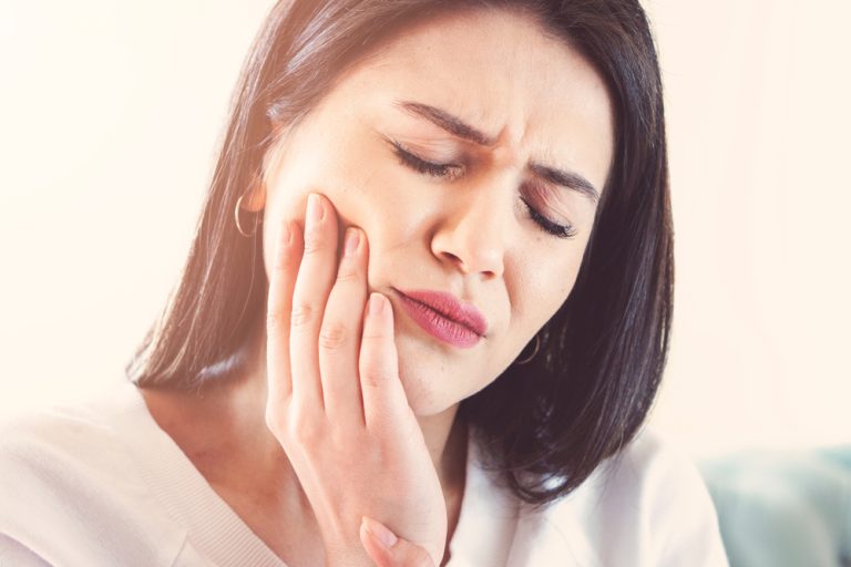Woman experiencing tooth pain, touching her cheek, reflecting temporary sensitivity or discomfort related to dental treatments.