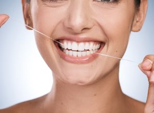 Smiling woman using dental floss to maintain oral hygiene, emphasizing the importance of flossing for porcelain veneers care.