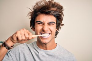 Young man brushing teeth with a toothbrush, demonstrating proper daily care for dental veneers and overall oral health.