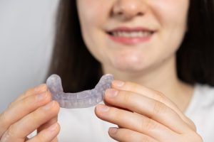 Smiling woman holding a clear dental mouthguard, promoting dental care and sensitivity management during winter.