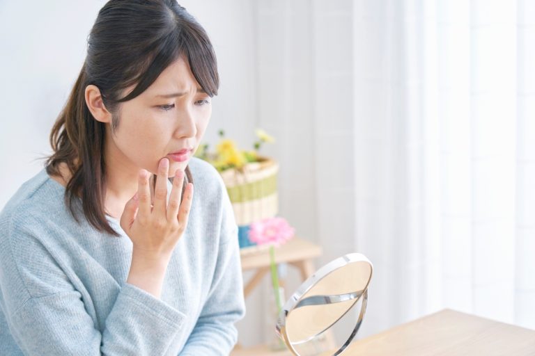 Woman experiencing tooth pain while looking in a mirror, reflecting concerns about oral health and dental issues.