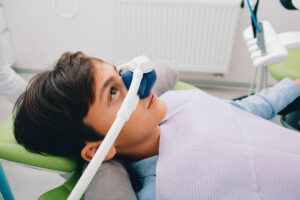 Child receiving nitrous oxide sedation in dental office, wearing a dental bib and relaxed during treatment.