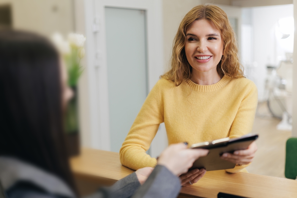woman turning in paperwork at front desk of dental office