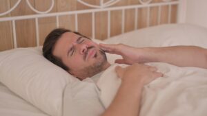 man dealing with toothache at night in bed