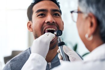 Patient receiving dental examination from a dentist using an otoscope, highlighting the importance of professional dental care for veneer maintenance at Lexington Dental of Owasso.